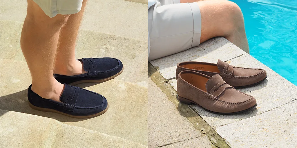 Man standing wearing navy suede Loake loafers on a sun drenched terrace, in nylon grey shorts. Shoes shown are Lucca in navy suede leather